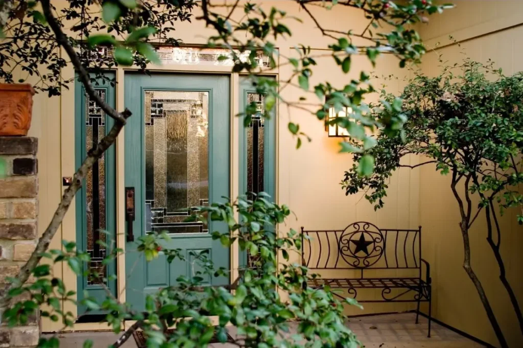 Entrée de maison avec porte verte à vitraux, applique murale et banc en fer forgé, ambiance chaleureuse